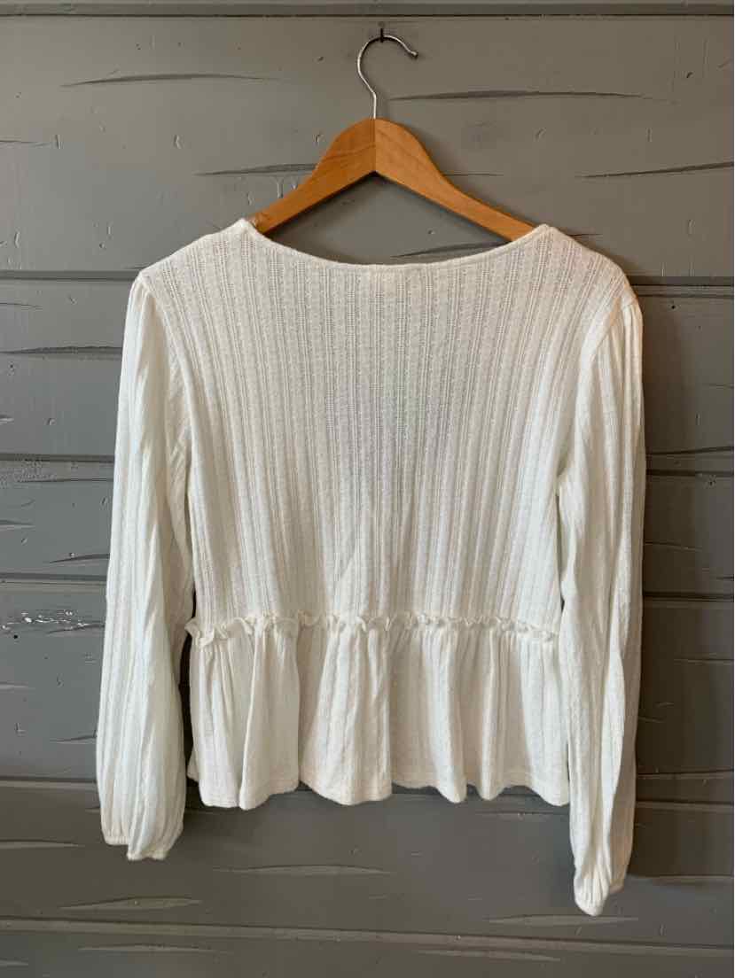 White long-sleeve ribbed knit top with peplum waist and round neckline hanging on wooden hanger.
