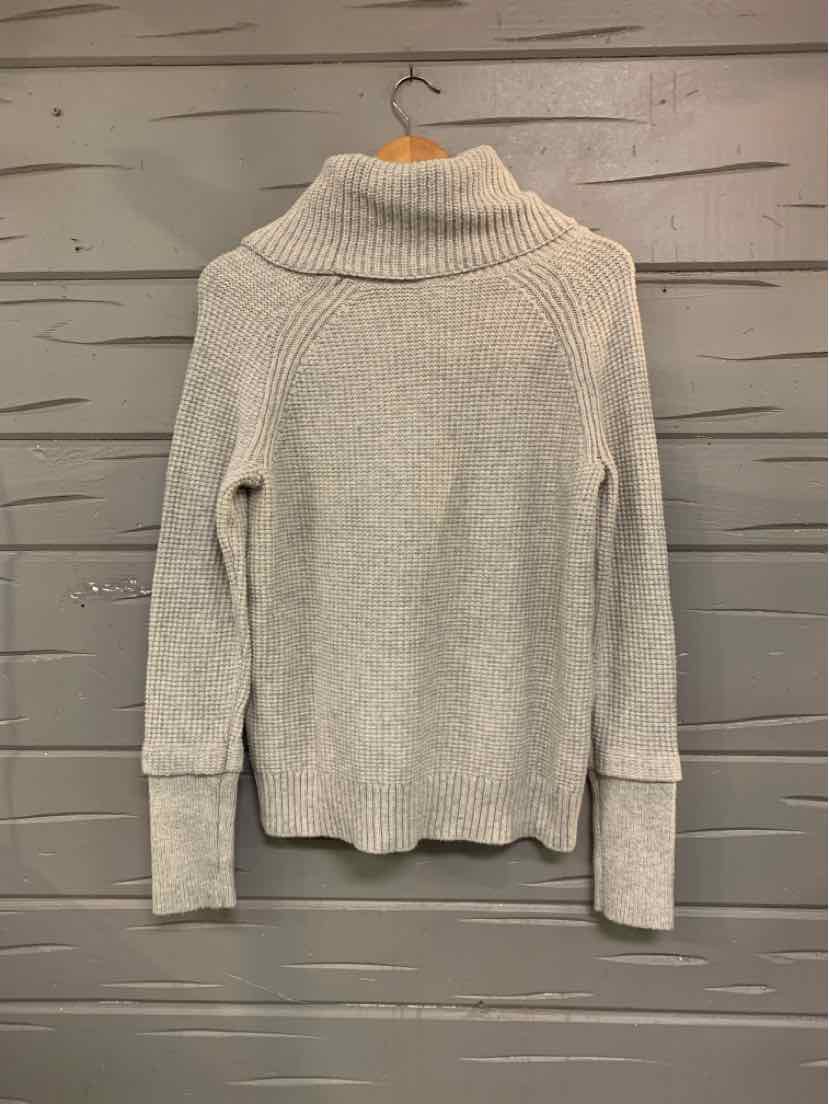 Light gray knit turtleneck sweater with long sleeves and ribbed cuffs hanging on wooden hanger.
