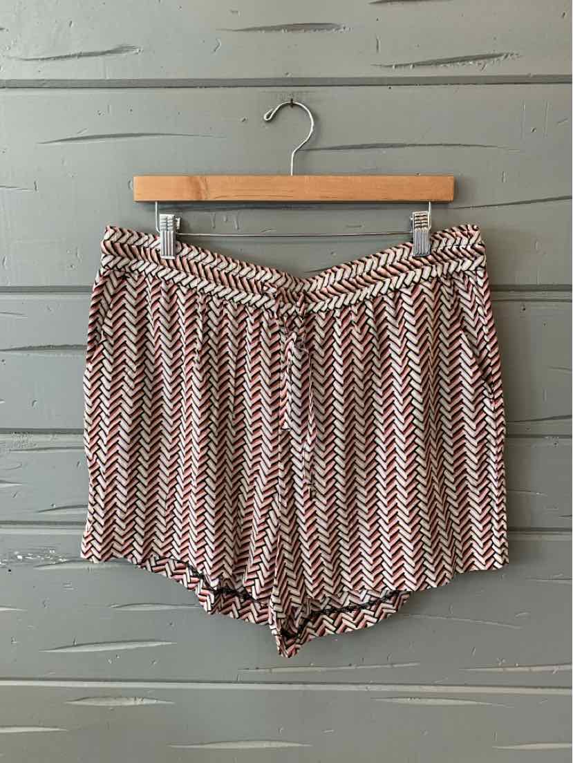 Mauve chevron-patterned loose-fitting shorts with an elastic waistband on wooden hanger against gray wooden wall.