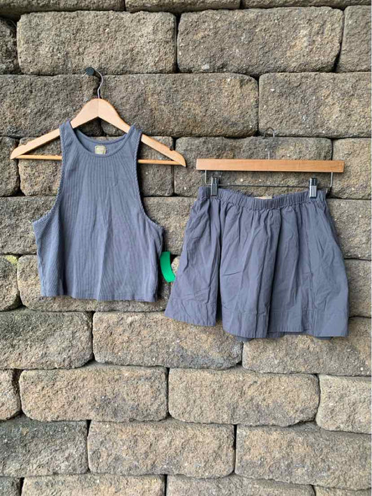Gray sleeveless cropped tank top and matching loose shorts set hanging on wooden hangers against a stone wall background.
