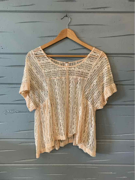 Nude lace short-sleeve blouse with loose fit and scoop neckline on wooden hanger.