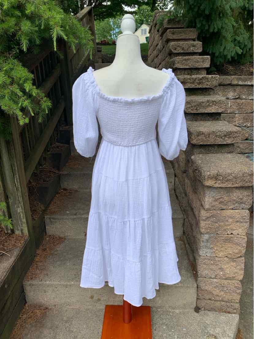 White midi dress with puffed elbow-length sleeves and a smocked square neckline and waist, tiered skirt design.