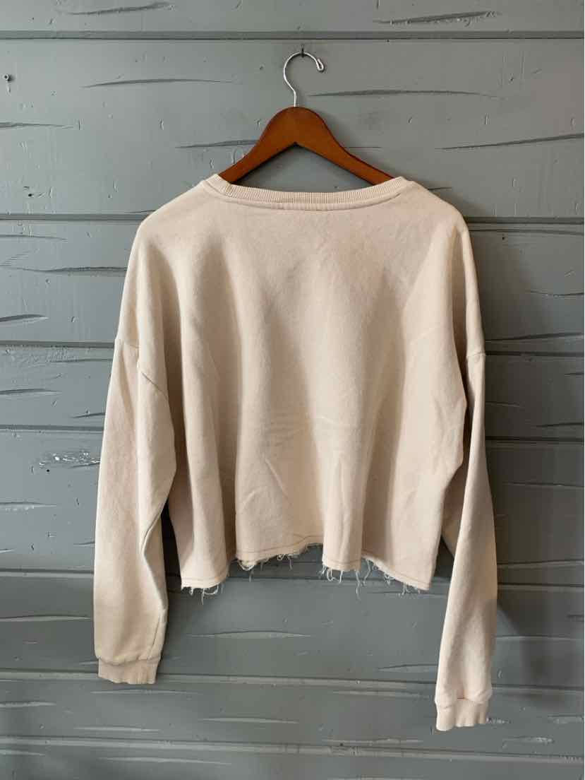 Light beige long-sleeve cropped sweatshirt with raw hem and relaxed fit on wooden hanger against gray shiplap background.