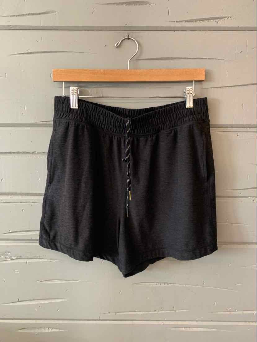 Black mid-length athletic shorts with elastic waistband and adjustable drawstring hanging on wooden hanger against light.