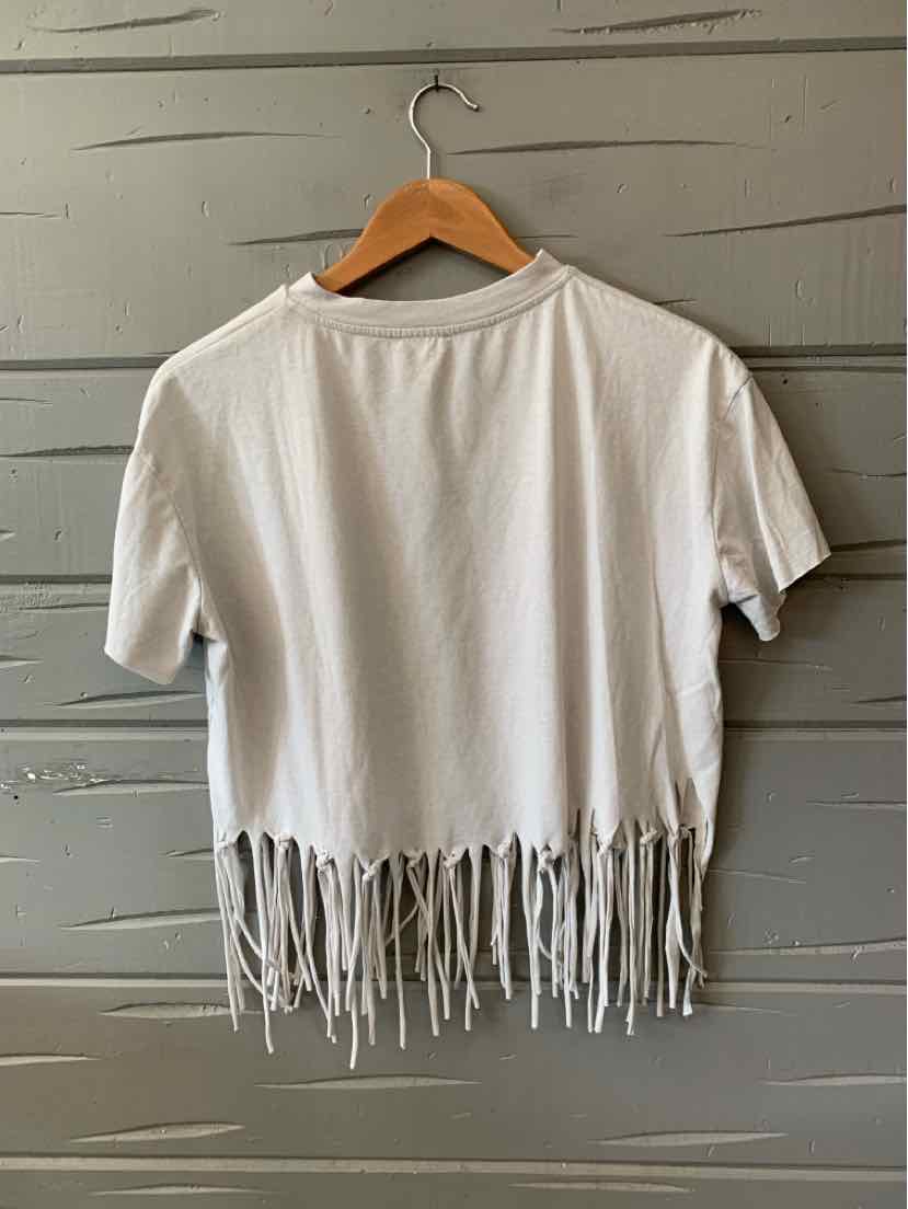 White short-sleeve crop top with fringe hem hanging on wooden hanger.
