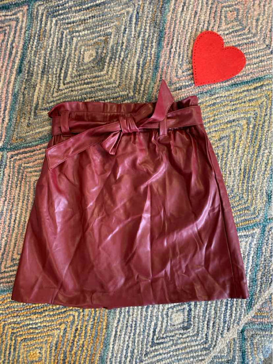 Burgundy leather skirt with paperbag waist and tie belt on patterned rug with red heart decor.
