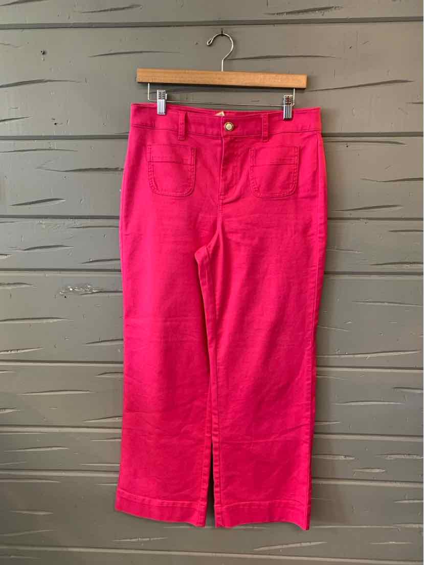 Bright pink cropped pants with front pockets and button closure hanging on wooden hanger.