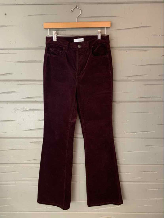 Dark burgundy velvet wide-leg pants with a button closure, hanging from a wooden clip hanger.