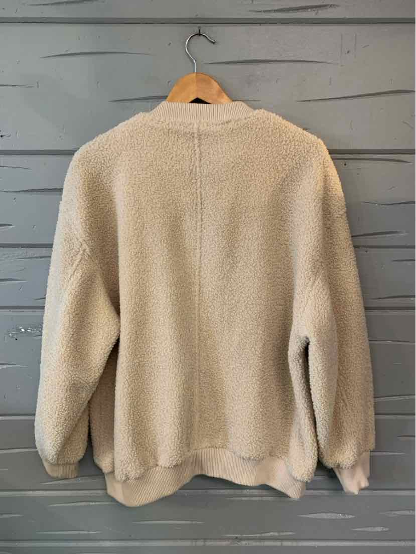Tan textured knit sweater hanging on a wooden hanger, with long sleeves and a ribbed hem.