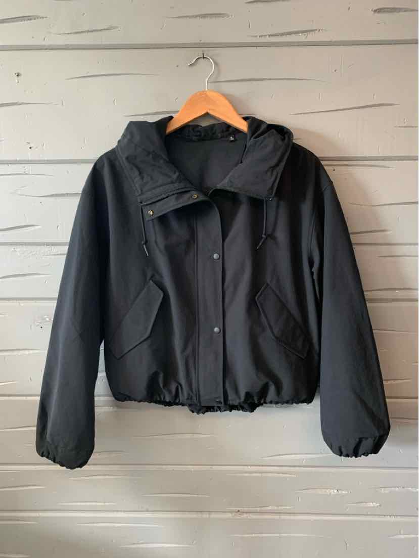 Black lightweight hooded jacket with elastic cuffs and hem hanging on wooden hanger.