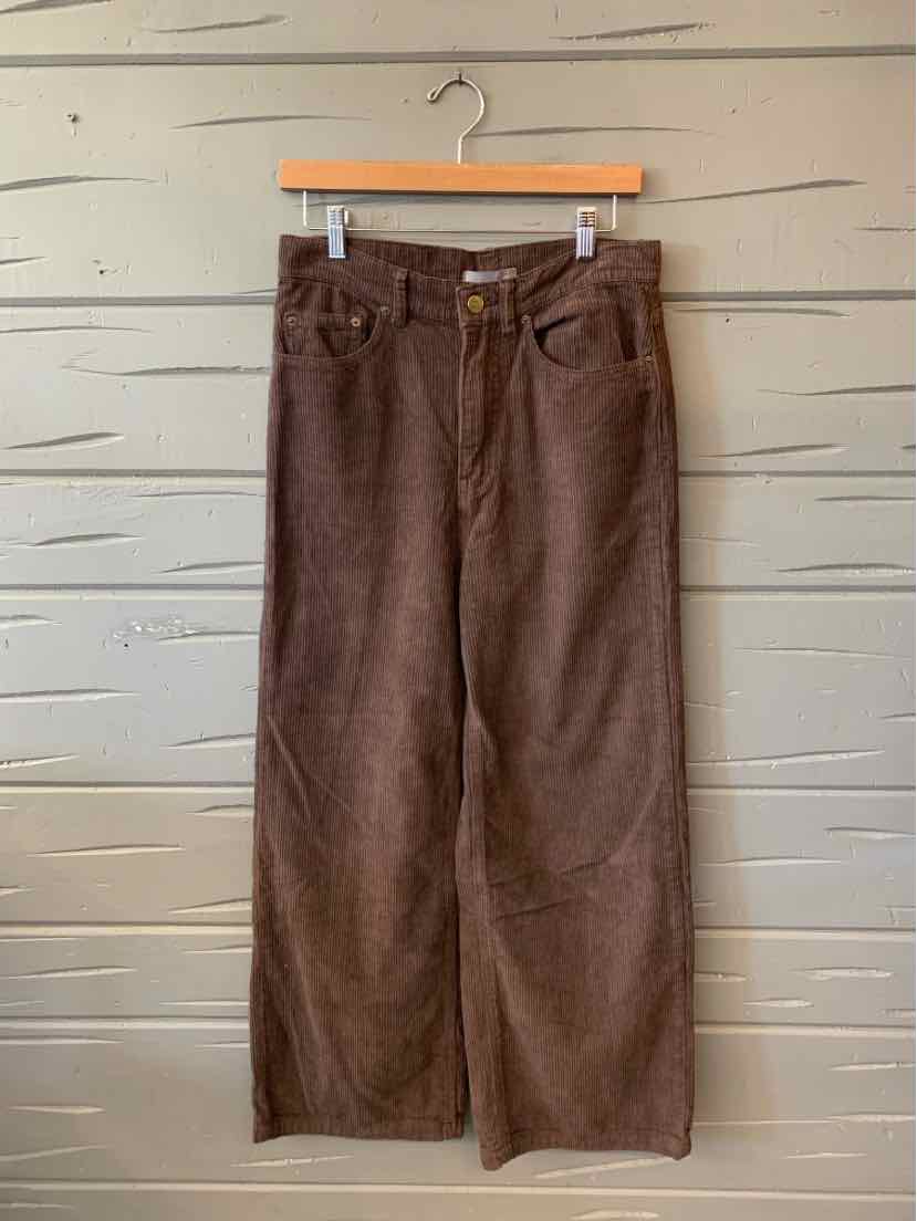Brown corduroy wide-leg pants with a high waist, front pockets, and button closure, hanging from a wooden hanger.