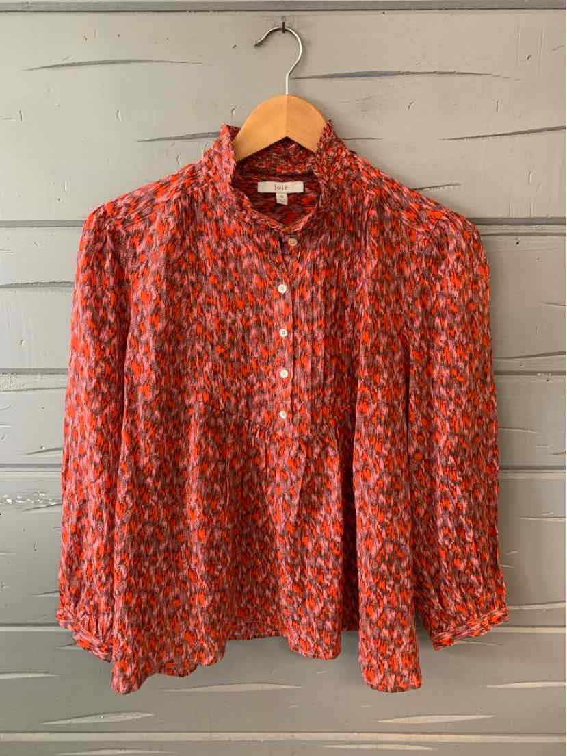 Orange and pink patterned lightweight blouse with long sleeves and a gathered neckline on a wooden hanger.