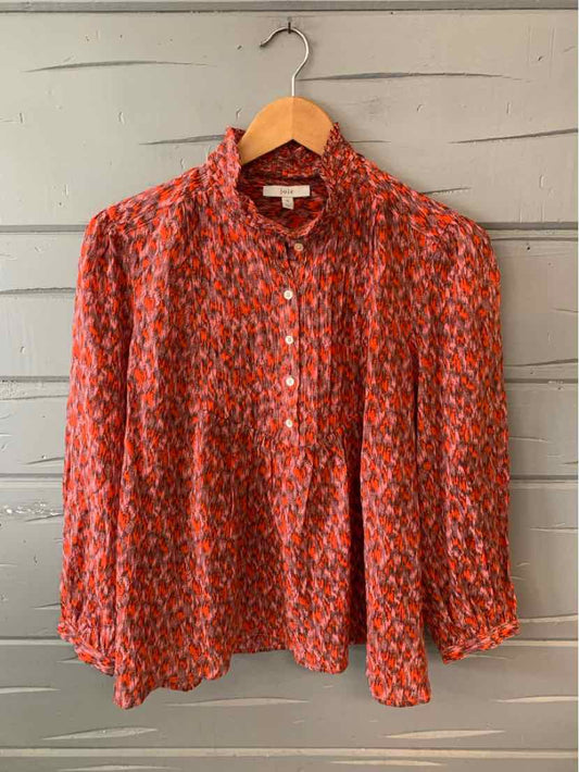 Orange and pink patterned lightweight blouse with long sleeves and a gathered neckline on a wooden hanger.