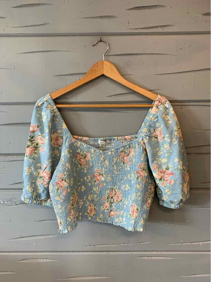 Light blue floral blouse with puffed sleeves and square neckline on wooden hanger.