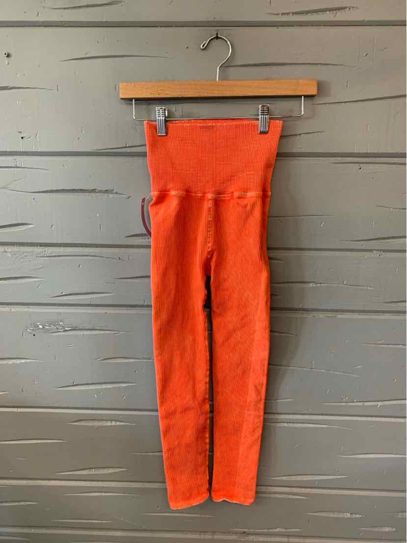 Bright orange high-waisted leggings with textured fabric and a wide waistband hanging on a wooden hanger.