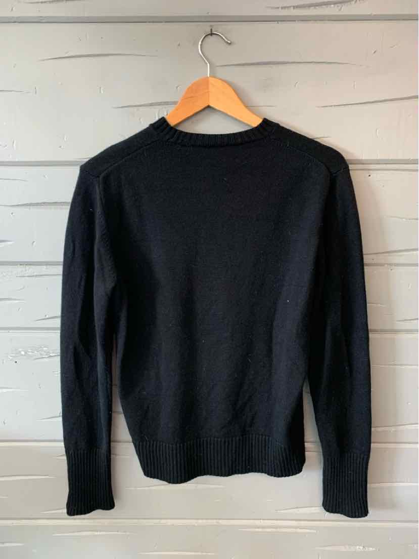 Black long-sleeve crewneck sweater with fitted silhouette hanging on wooden hanger.