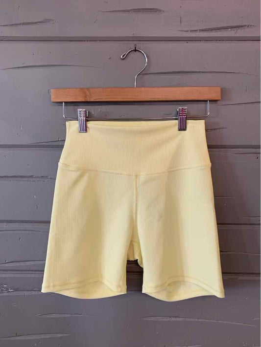 Light yellow high-waisted biker shorts with wide waistband hanging on wooden hanger against gray wall.