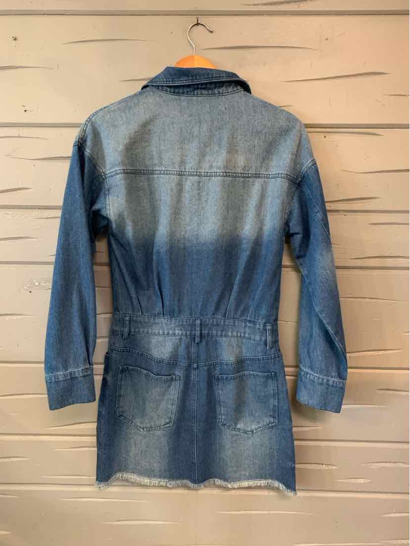 Blue denim long-sleeve dress with a cinched waist and frayed hem hanging on wooden wall.