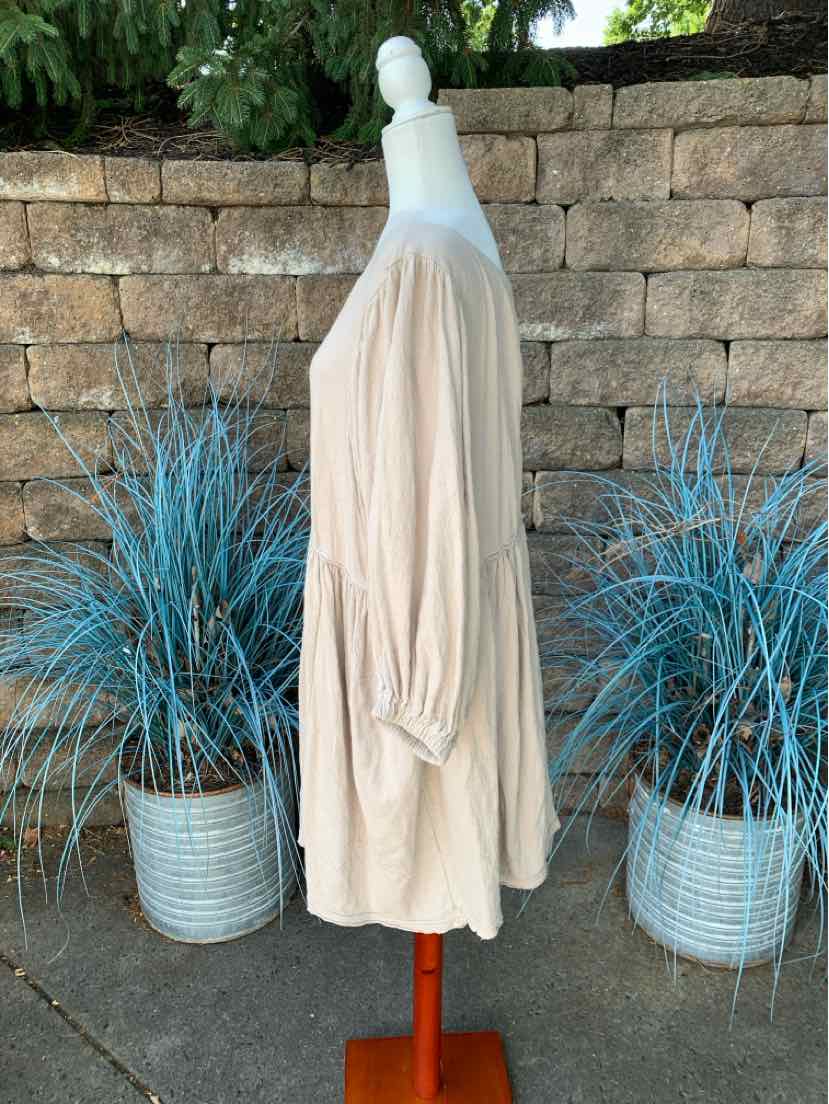 Beige loose-fit long-sleeve blouse with gathered cuffs and a flowy hem on a white mannequin.
