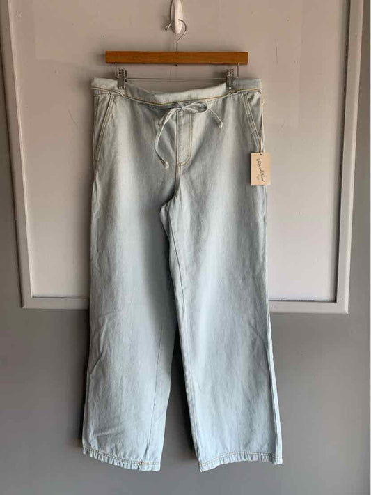 Light blue wide-leg denim pants with drawstring waist hanging on wooden hanger against white wall.