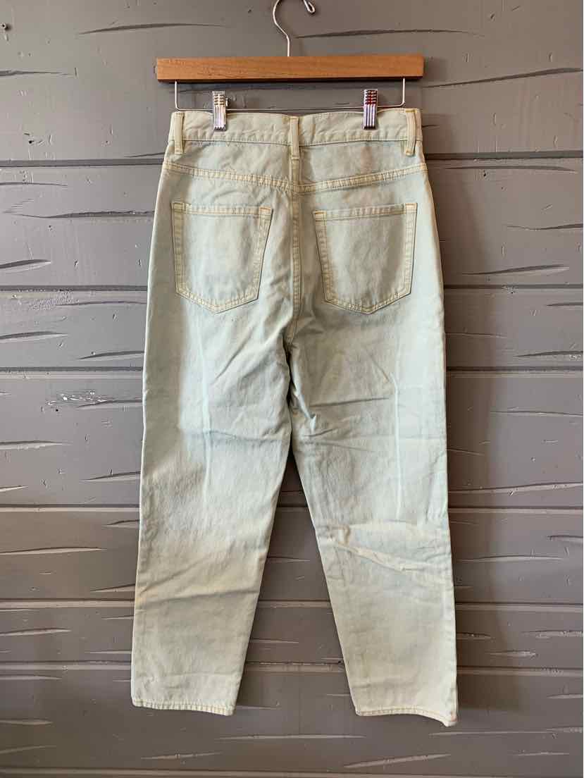 Light wash denim jeans with straight legs and two back pockets hanging on wooden hanger against gray shiplap wall.