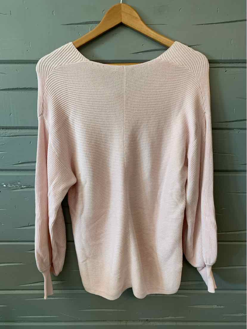 Light pink long-sleeve knit top with round neckline and ribbed cuffs on wooden hanger.