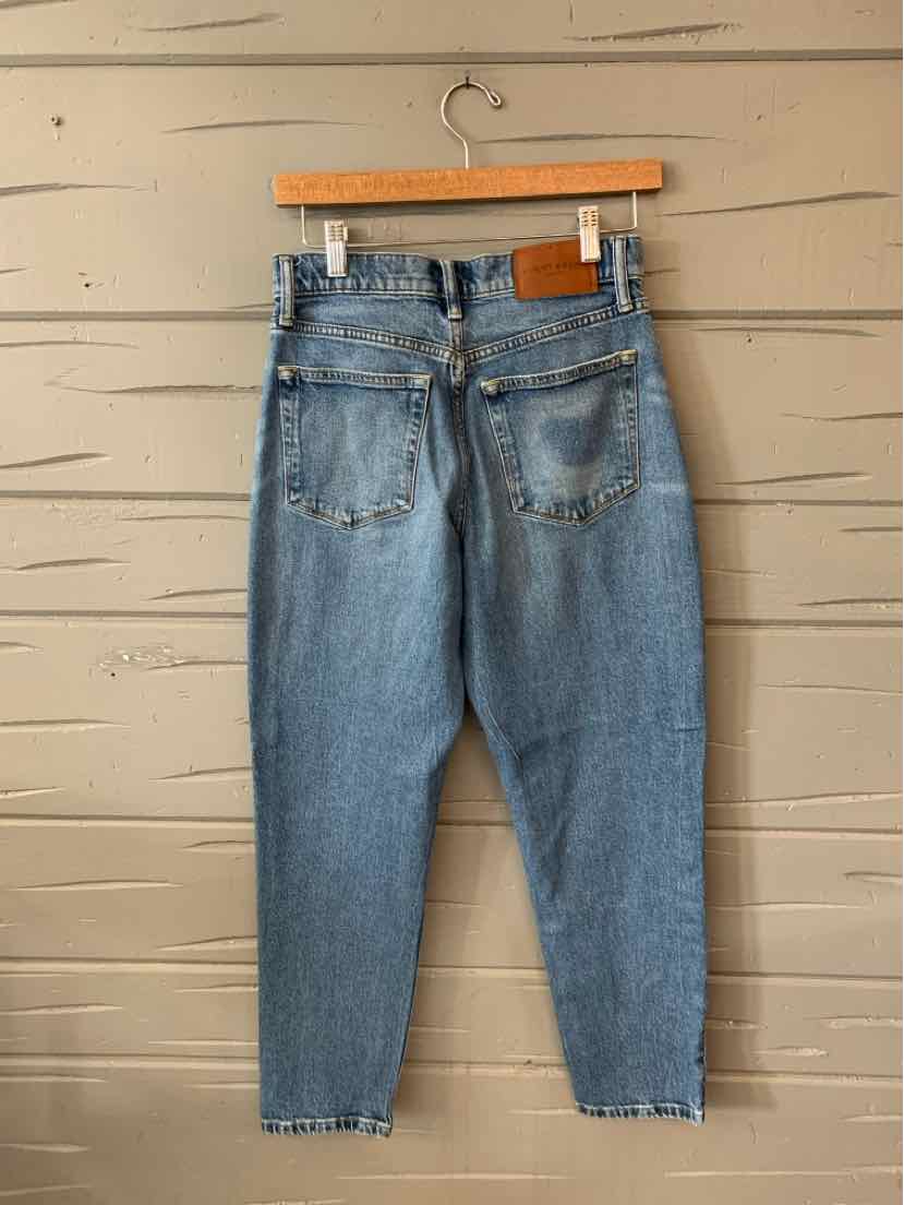 Light wash blue denim jeans with high waist, tapered legs, and back patch pockets hanging on wooden hanger.