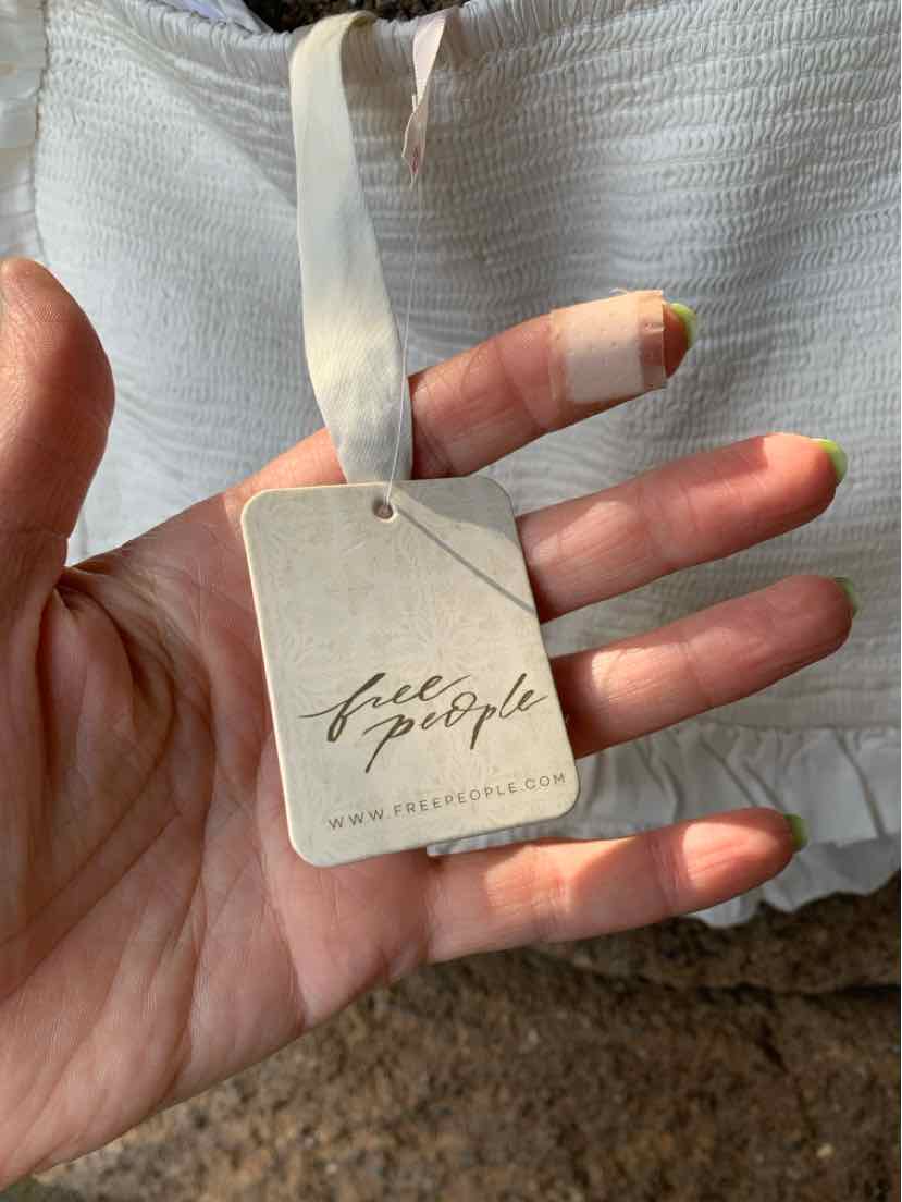 White textured fabric dress with a cream ribbon tie and a Free People brand tag attached.