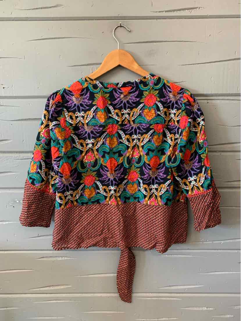 Multicolor Maeve cardigan with vivid floral embroidery and textured red-brown knit trim, hanging on a wooden hanger.