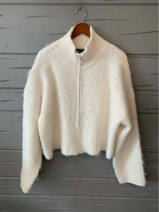 Ivory white fuzzy cropped zip-up jacket with a high collar and long sleeves, hanging on a wooden hanger.