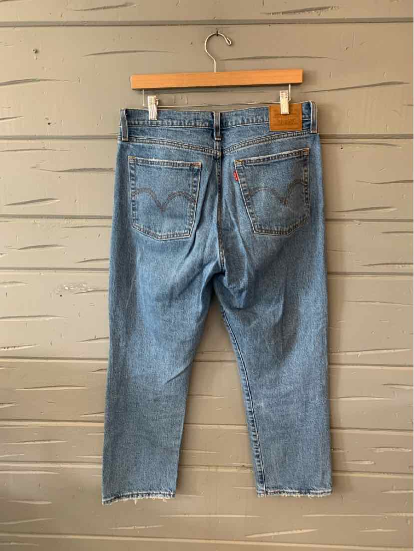 Light blue denim Levi's jeans size 10 with raw hem and classic five-pocket styling hanging on wooden hanger.