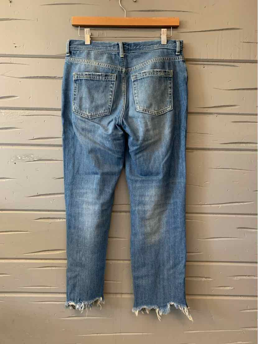Blue denim jeans with frayed hems and back pockets hanging on wooden hanger.