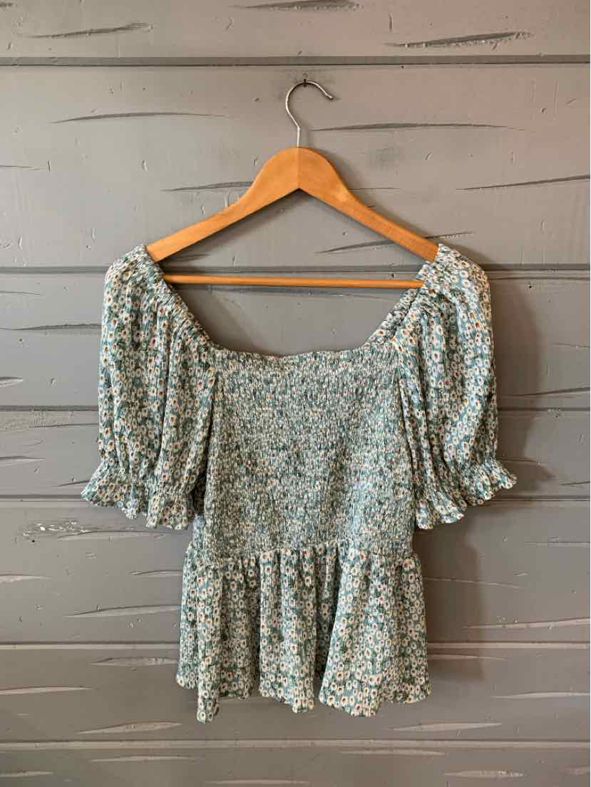 Light blue floral blouse with puff sleeves, smocked bodice, and peplum hem on wooden hanger.