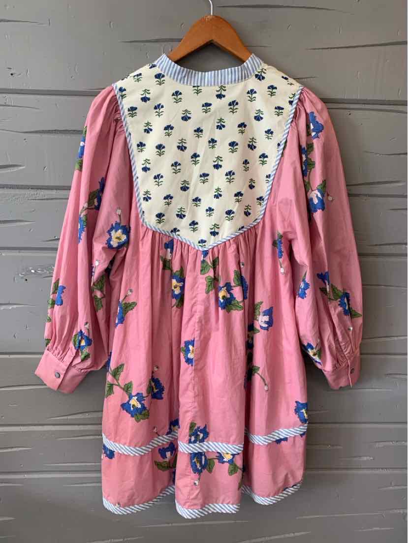 Pink long-sleeve floral dress with white bib featuring small blue flowers and gathered waist.