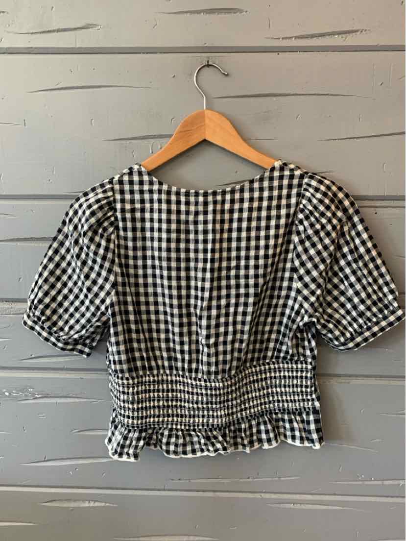 Black and white gingham puff sleeve blouse with smocked waist and ruffled hem on wooden hanger.