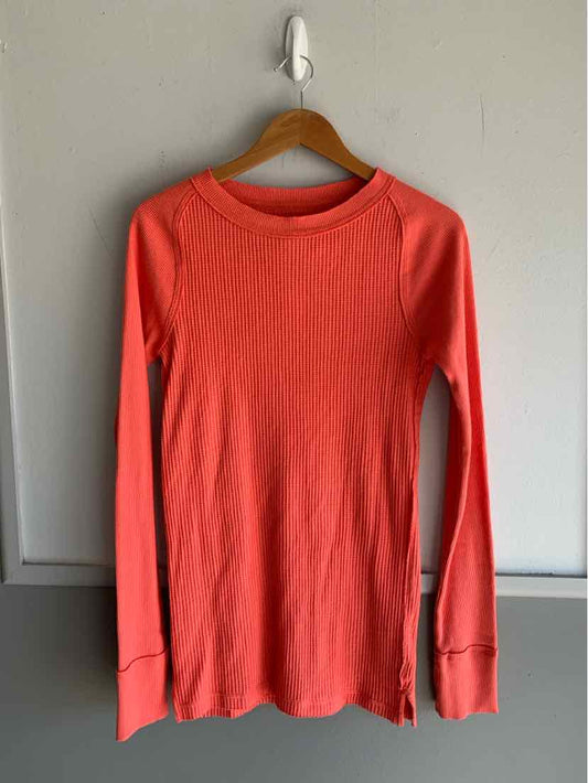 Long-sleeve coral ribbed top with crew neck and side slits on wooden hanger.