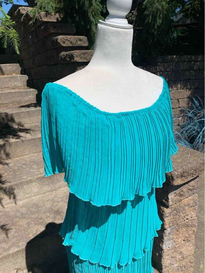 Teal off-shoulder pleated top with layered ruffles and short sleeves on a mannequin.