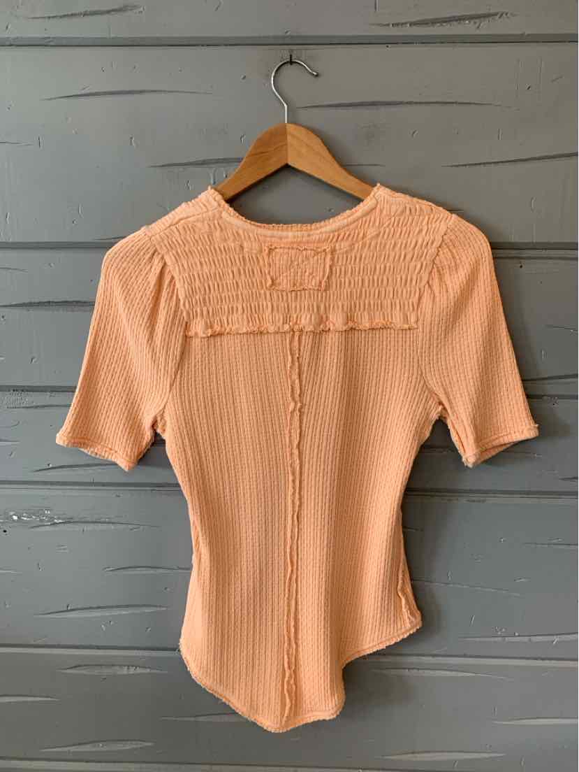 Peach ribbed short-sleeve top with a ruffled square neckline detail on wooden hanger.