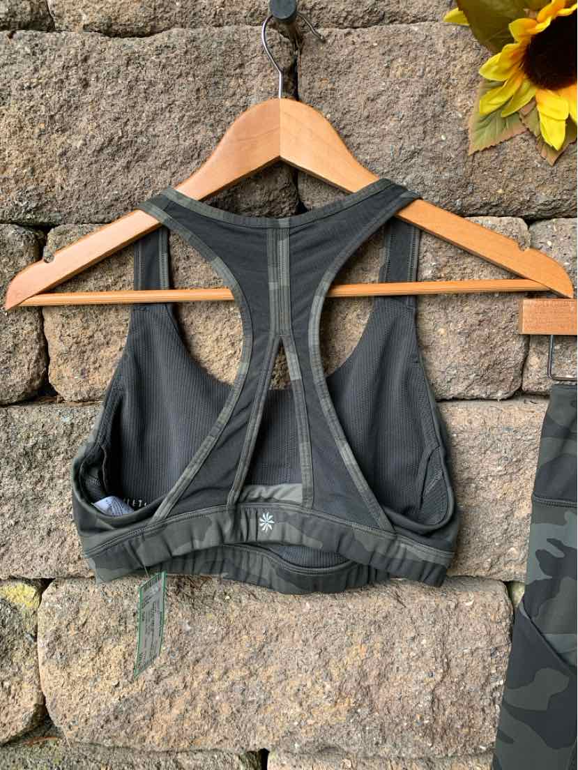Dark green camo sports bra with racerback design and elastic band bottom hanging on wooden hanger.