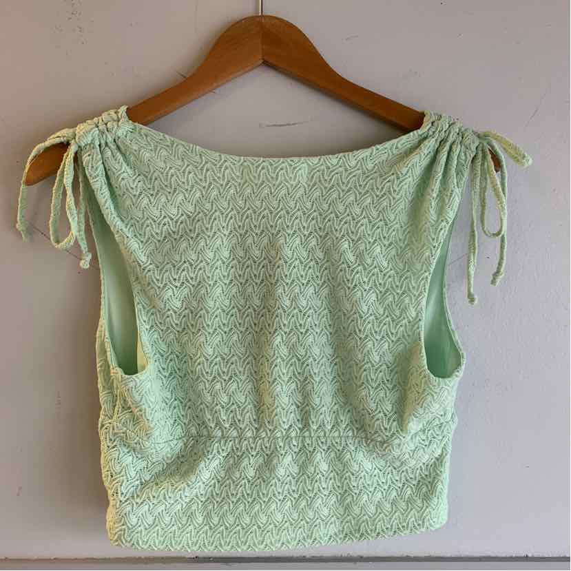 Mint green knitted sleeveless top with drawstring ties on shoulder straps hanging on wooden hanger.