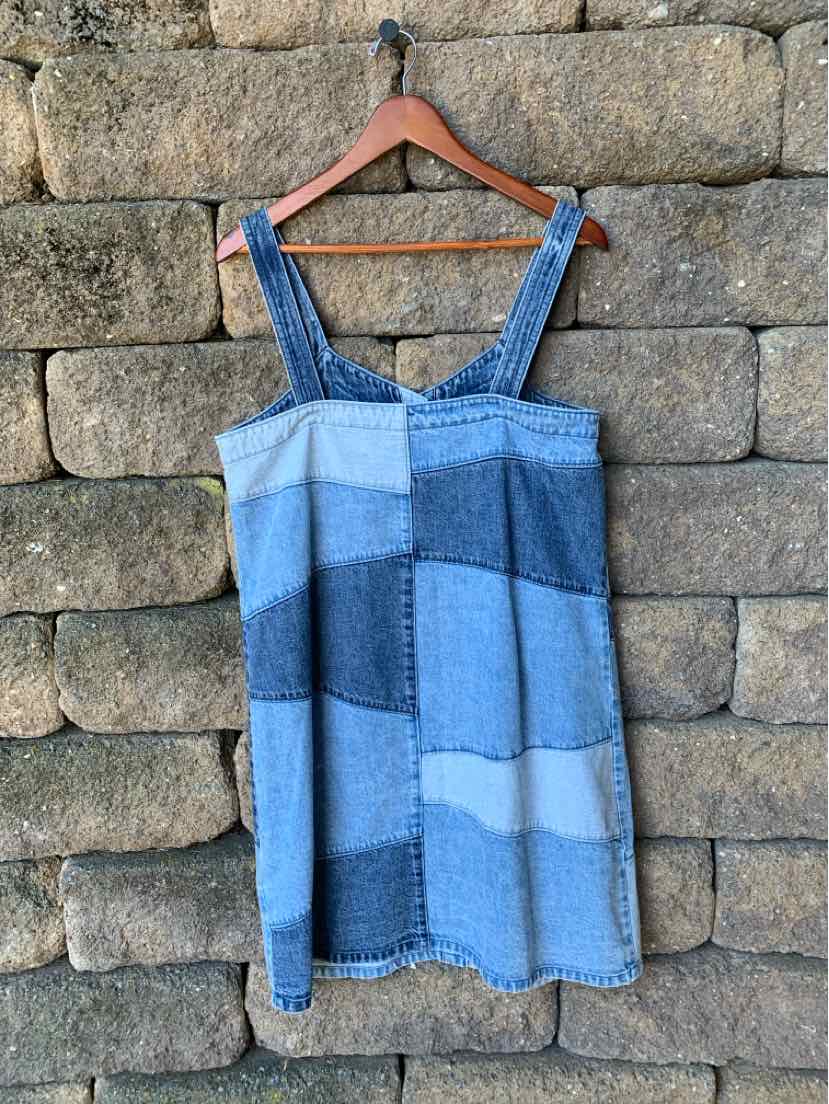 Blue patchwork denim dress with wide straps and straight neckline hanging on wooden hanger.