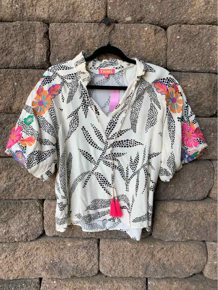 Lightweight white blouse with black leaf patterns, colorful floral accents on sleeves, and a front tassel tie.
