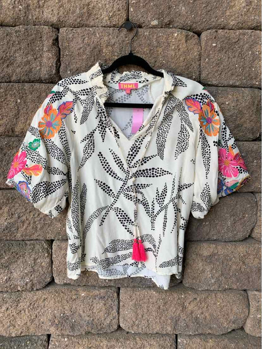 Lightweight white blouse with black leaf patterns, colorful floral accents on sleeves, and a front tassel tie.