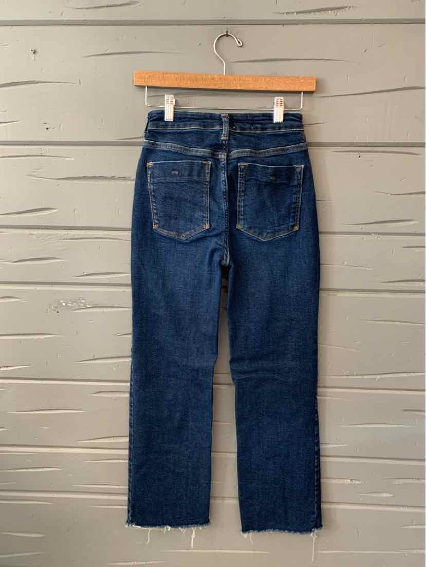 Dark blue denim jeans with straight legs, raw hem detailing, and back pockets hanging on wooden hanger.