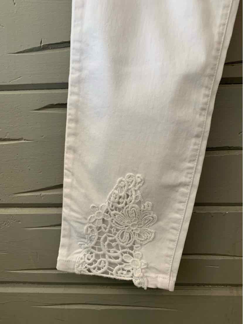 White pants leg with delicate floral lace embroidery near the hem, slim fit, smooth fabric.