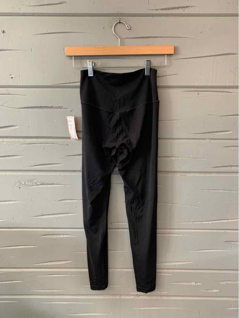 Black slim-fit leggings with high waistband hanging on wooden hanger against gray wooden panel background.