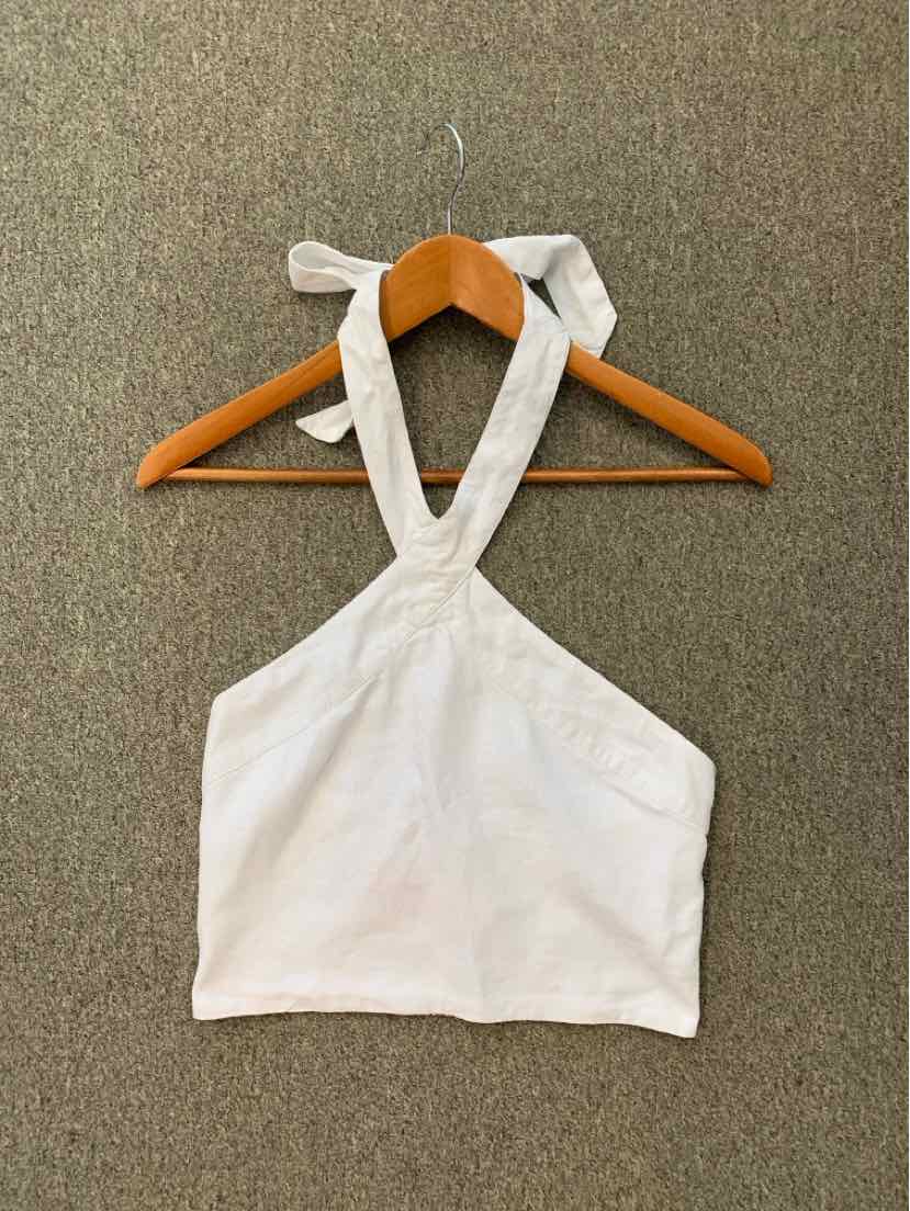 White halter crop top with tie neck straps and a straight hem, hung on wooden hanger.