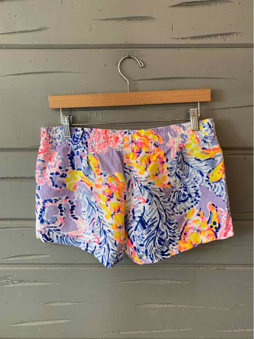 Colorful floral and leaf patterned women's shorts with pink, orange, blue, and white tones, hung on wooden hanger.