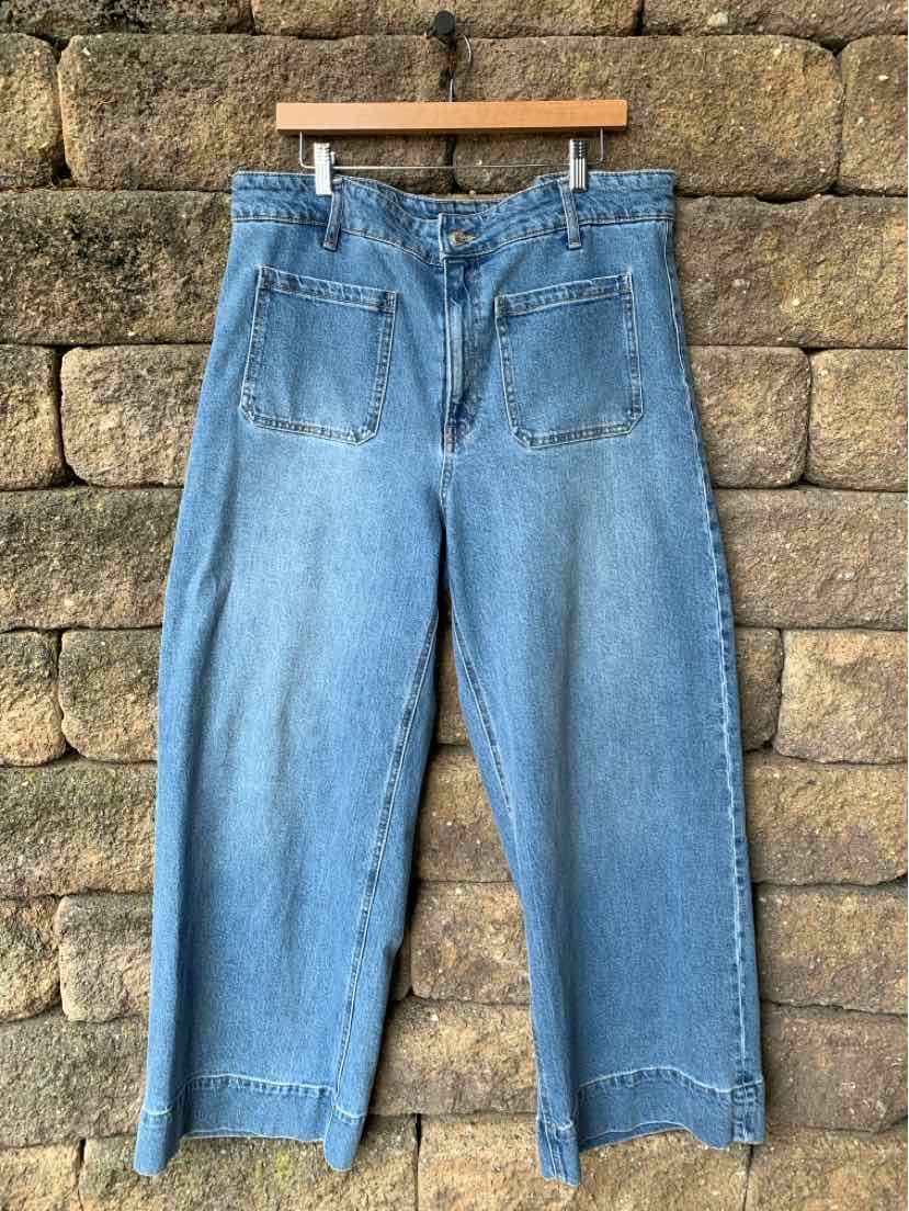 Light blue wide-leg denim jeans with high waist and back patch pockets hanging on wooden hanger.