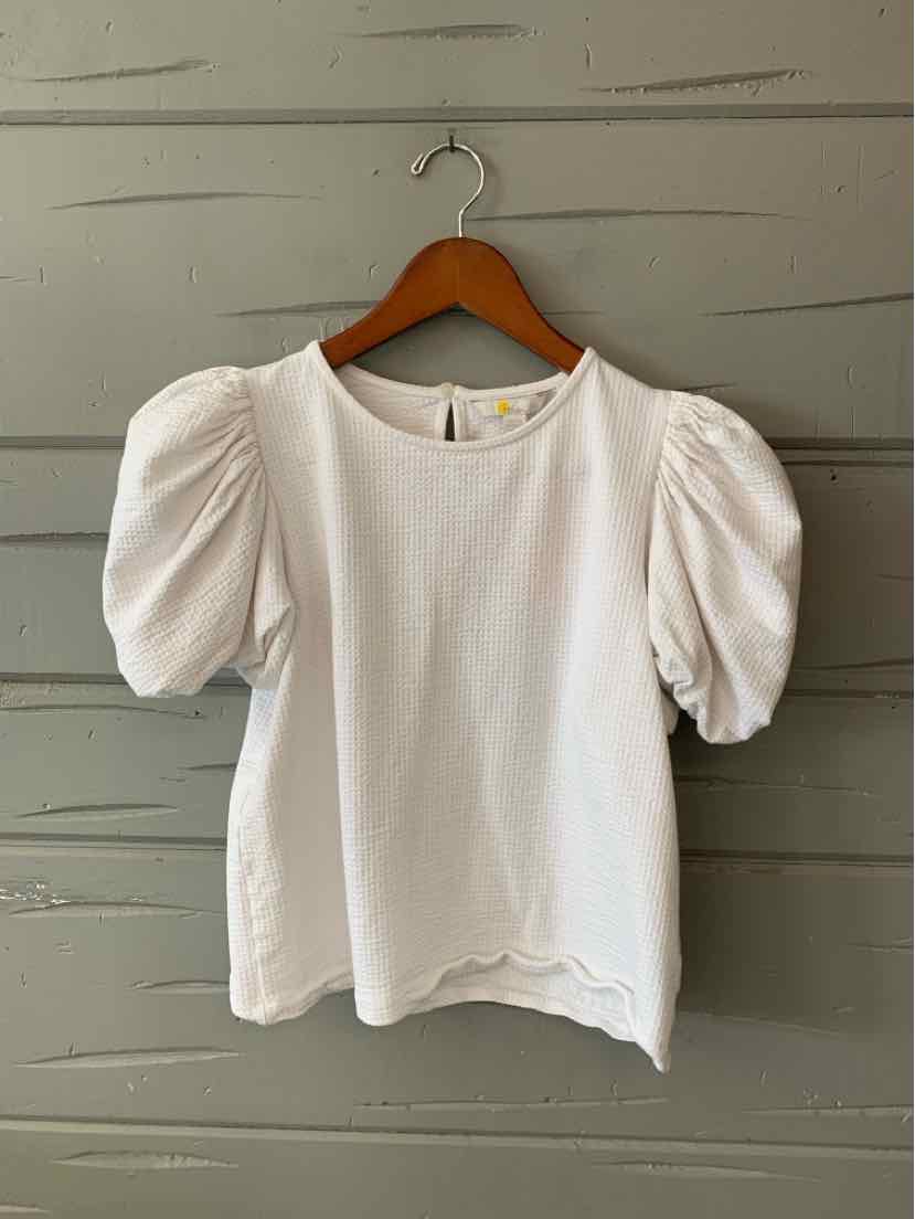 White blouse with puffed short sleeves and round neckline hanging on wooden hanger against gray wall.